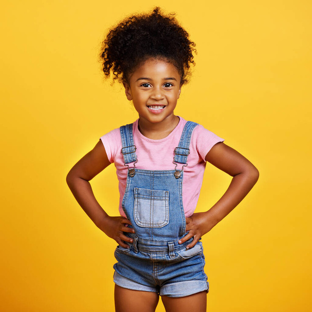 Studio portrait mixed race girl looking standing with her hands on her hips isolated against a yellow background. Cute hispanic child posing inside. Happy and cute kid smiling and looking confident. - Zdjęcie, obraz