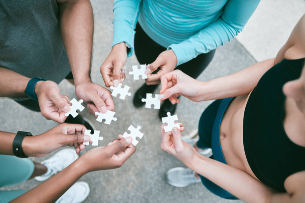 Closeup of diverse group of people from above assembling jigsaw puzzle pieces together. Hands of multiracial people working in synergy to problem solve. Using dedicated teamwork to support and help - Foto, afbeelding