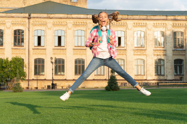 Happy energetic teen girl jumping in school yard outdoors, Knowledge day. - Foto, afbeelding