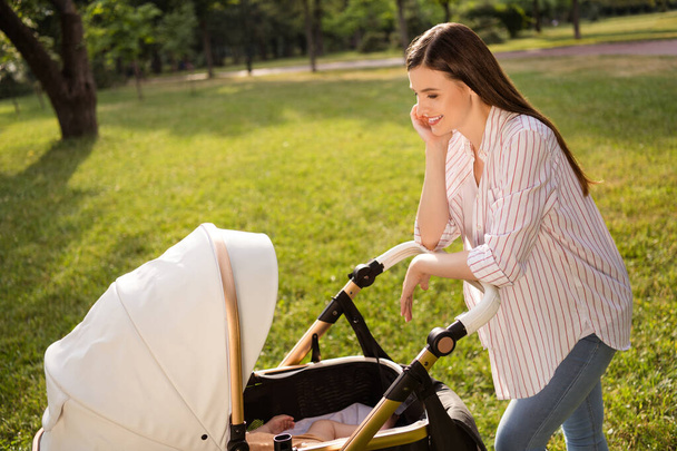 Photo of charming funny mother dressed casual clothes smiling enjoying sunny walk admiring little son outdoors backyard. - 写真・画像