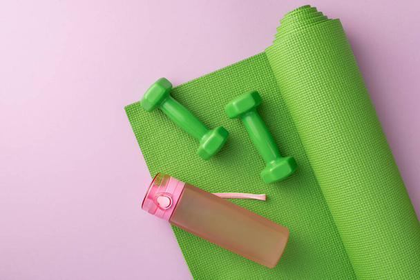 スポーツアクセサリーのコンセプト。緑の運動マットのダンベルと孤立したパステルライラックの背景に水のピンクのボトルのトップビューの写真 - 写真・画像