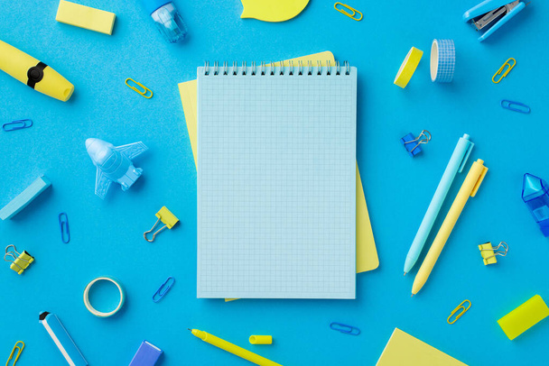Back to school concept. Top view photo of school accessories adhesive tape sharpeners stapler erasers binder clips corrector marker pens and notepads on isolated blue background with blank space - Foto, imagen