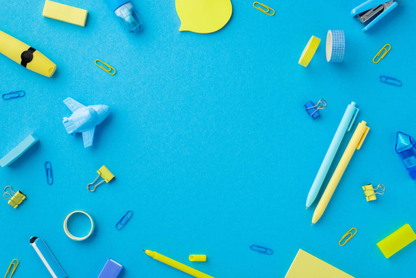 Back to school concept. Top view photo of yellow and blue stationery adhesive tape sharpeners stapler erasers binder clips corrector marker pens isolated blue background with empty space in the middle - Foto, Imagen