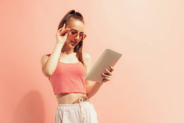 Looking at device screen. One young charming girl using digital tablet isolated on peach color background. Concept of beauty, art, fashion, emotions, youth. Copy space for ad - Photo, Image