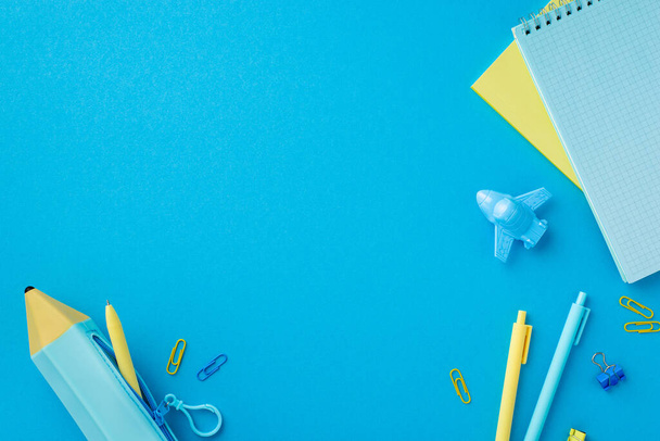Back to school concept. Top view photo of yellow and blue stationery copybooks pens plane shaped sharpener binder clips and pencil-case on isolated blue background with empty space - Photo, Image