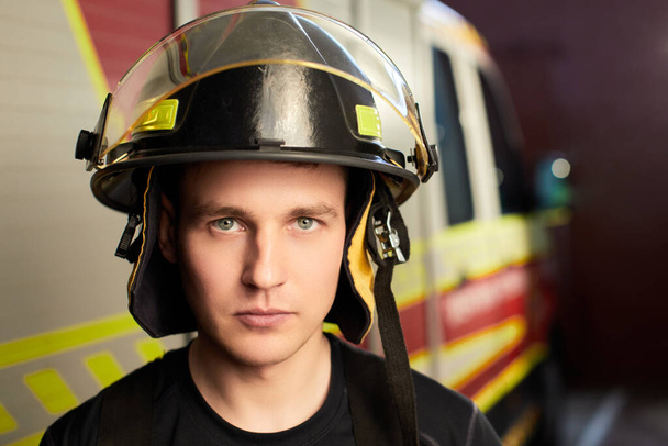 Brandweerman in uniform en helm staan achter van brandweerwagen  - Foto, afbeelding