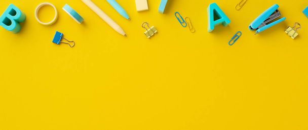 School accessories concept. Top view photo of plastic alphabet letters stapler adhesive tape erasers binder clips and pens on isolated yellow background with empty space - 写真・画像