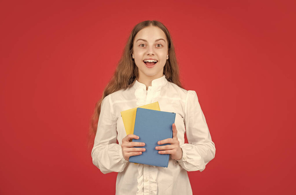 amazed child in white shirt ready to study do homework with book on red background, back to school. - Фото, изображение
