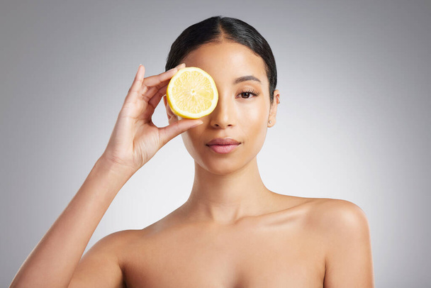 Studio Portrait of a beautiful young mixed race woman holding a lemon. Hispanic model using a lemon for oil control against a grey copyspace background. - 写真・画像