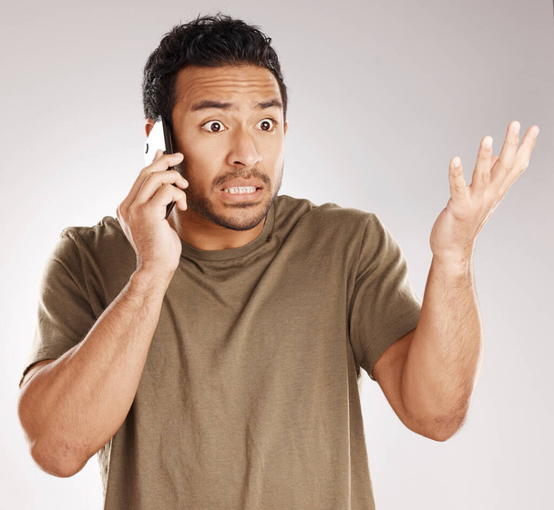 Handsome young mixed race man looking irritated, aggravated or agitated while using his phone in studio isolated against a grey background. Displeased hispanic male making a call to complain or argue. - Foto, Imagen