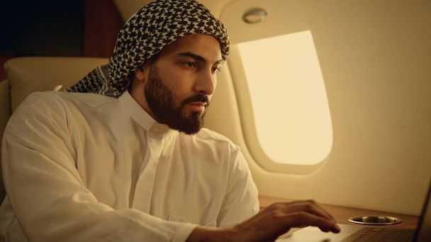 Koncentrált üzletember laptoppal a repülőgépen. Komoly ember, aki netezik luxusgépen. Jóképű arab pénzügyi menedzser, aki számítógépet néz az üzleti úton. Férfi szakmai koncepció. - Fotó, kép