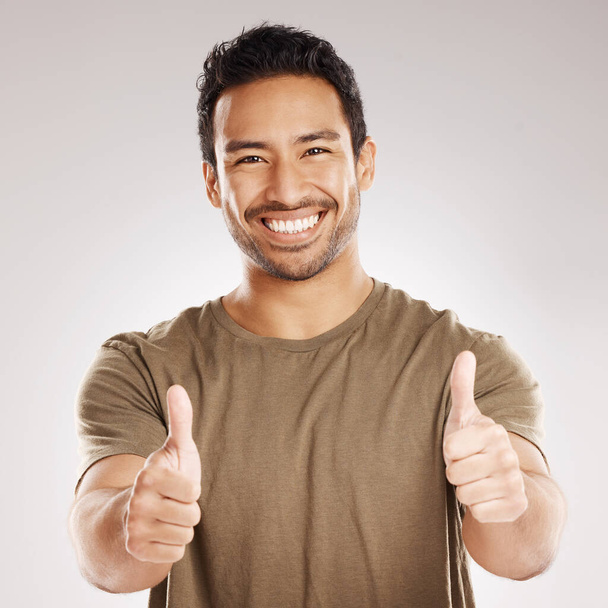 Handsome young mixed race man giving thumbs up while standing in studio isolated against a grey background. Hispanic male showing support or appreciation. Backing or endorsing a product or company. - Foto, Imagem