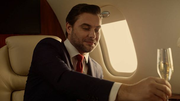 Smiling entrepreneur relaxing jet closeup. Attractive drink champaign sunlight. Rich handsome man confident company executive look watch talk partner wife on corporate trip. Wealthy lifestyle concept - Zdjęcie, obraz