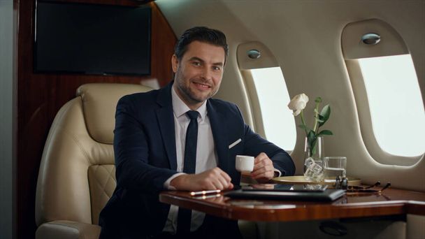 Smiling ceo posing alone at airplane window. Successful man enjoy corporate trip looking porthole. Confident stylish businessman flying luxury first class in suit. Elegant gentleman resting on journey - Photo, Image