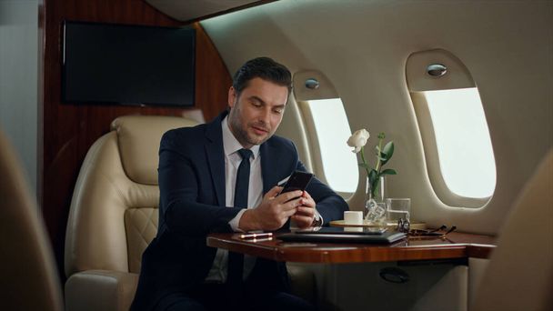 Druk bezig met bellen in een luxe jet. Gericht manager drinken koffie reizen business class vliegtuig. Knappe zakenman die het mobiele gesprek beëindigt. Geslaagde financieel analist praten cel - Foto, afbeelding