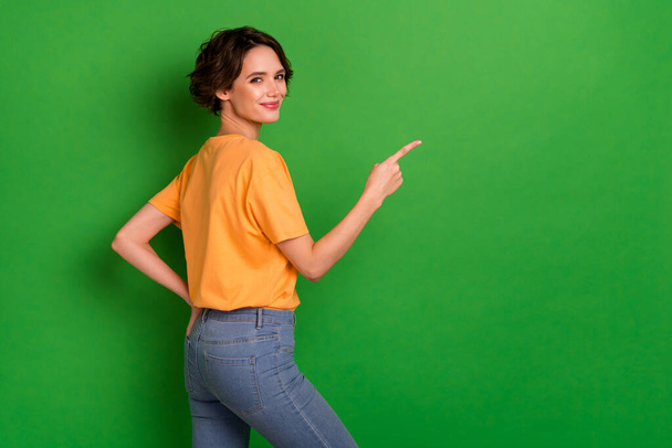 Photo of cute positive young lady wear orange outfit smiling pointing empty space isolated green color background. - Fotó, kép