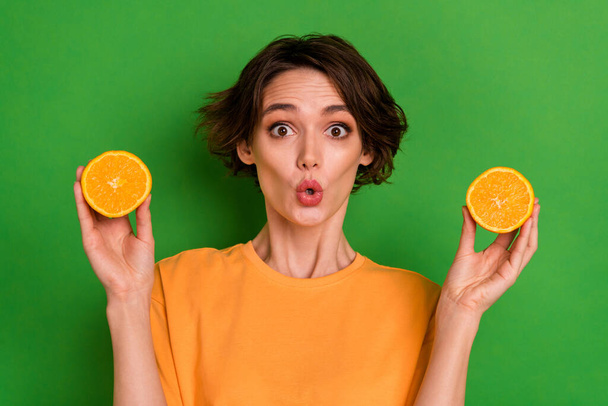Photo of impressed funky young lady wear orange outfit holding citrus halves isolated green color background. - Foto, imagen