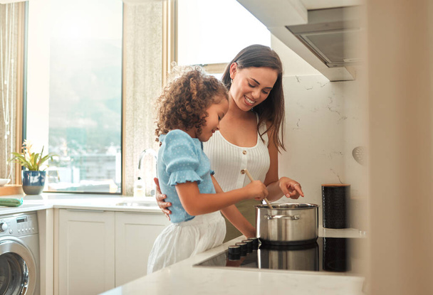 Мати і маленька донька готують вечерю вдома. Молода мати стояла з дочкою і допомагала їй під час перемішування їжі на плиті. Мама навчає маленьку дівчинку готувати
. - Фото, зображення