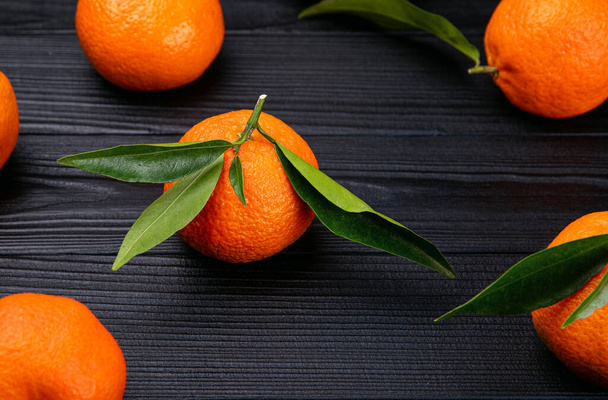 High angel view of whole ripe fresh citrus fruits tangerines with green leaves on black background or food pattern. - Photo, Image