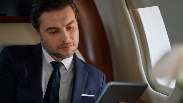 Successful manager tapping tablet in plane closeup. Focused ceo using computer checking online report in business class. Confident european businessman touch digital pad in jet. Corporate trip concept - Photo, Image
