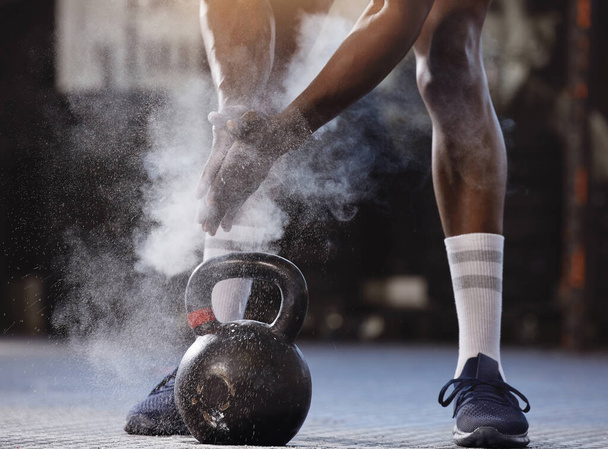 Closeup of unknown african american athlete using powder and chalk on hands before lifting kettlebell in gym. Strong, fit, active black man getting ready to workout. Weightlifting in exercise routine. - Foto, Imagem
