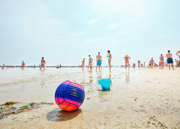Beach volley μπάλα σε μια ιταλική παραλία σε ένα ηλιόλουστο πρωινό του καλοκαιριού με τους ανθρώπους στο πίσω μέρος καθώς δροσίζονται από τη θάλασσα. Παραλία μπάλα από την Αδριατική θάλασσα, Ιταλία. - Φωτογραφία, εικόνα