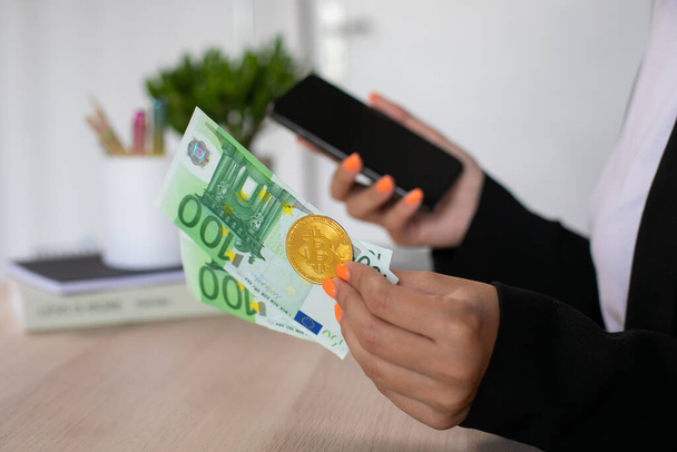 Euro bankovky a bitcoin na ženské ruce s telefonem na pracovišti. Kvalitní fotografie - Fotografie, Obrázek