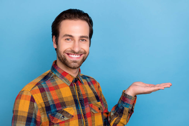 Photo of pretty cute young man wear plaid shirt arms hair smiling holding arm empty space isolated blue color background. - Fotografie, Obrázek