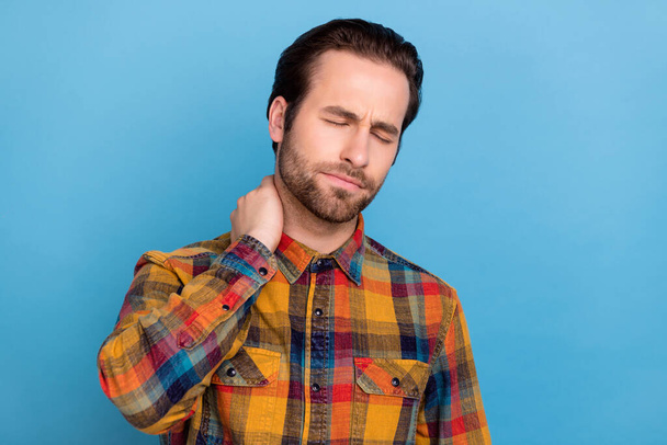 Photo of upset unhappy young man wear plaid shirt arm neck feeling tired isolated blue color background. - Foto, afbeelding