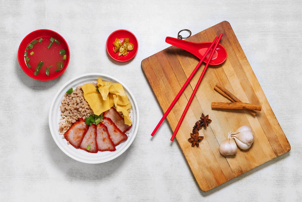 Sarawak Noodle Dry and Soup, Sarawak Mee Tai Bak and Sarawak Kway Teow in white bowl top view with raw garlic, spoon and chopsticks on wooden cutting board - Photo, Image