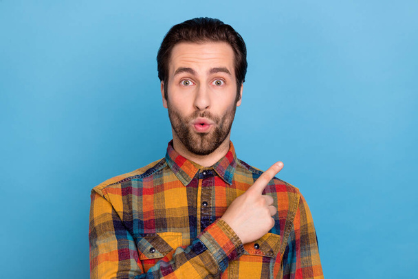 Photo of handsome impressed young guy dressed checkered shirt pointing finger empty space isolated blue color background. - Foto, Imagen