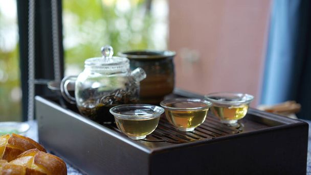 Hagyományos tea szett tálca modern átlátszó pot és tiszta kis csésze hangulatos kínai szobában. Természetes egészséges forró, áttetsző ital szárított levelekkel, jó aromát ad és piát ellazít.. - Fotó, kép