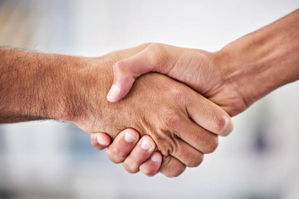 Closeup of two businessmen shaking hands in the office. Unknown mixed race professionals and colleagues sealing a deal with a hand gesture. Mixed race manager welcoming, promoting a business partner. - Foto, Imagen