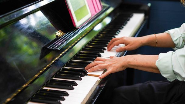 Yetişkin bir kadın, nota kağıdıyla elektronik piyano çalar. Akustik siyah piyanoda solo çalan profesyonel bir piyanist. Şarkı çalmayı öğreniyor ve pratik yapıyor. Klasik enstrüman. - Fotoğraf, Görsel