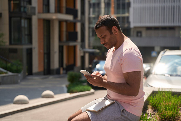 Serious focused man seated outdoors reading online news on smartphone touch screen - Foto, Bild