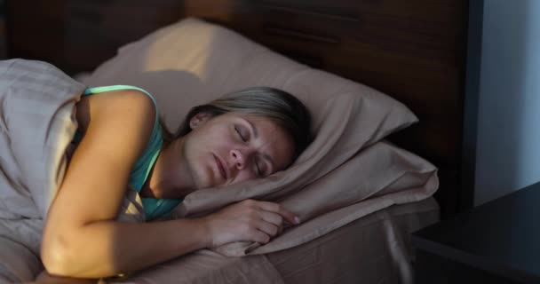 Ευτυχισμένη χαρούμενη γυναίκα ξυπνάει με τις πρώτες ακτίνες του ήλιου στο κρεβάτι. Θετική διάθεση και έννοια υγιούς ύπνου - Πλάνα, βίντεο