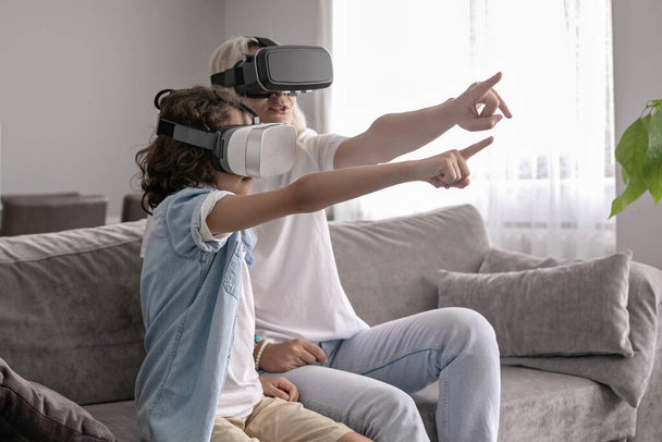 Mother and son wearing virtual reality headset vr glasses in living room at home having fun interacting with virtual reality playing games - Foto, afbeelding