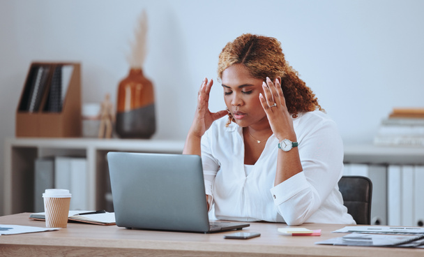 Stressed African American businesswoman making a mistake while using her laptop in the office. Professional black woman feeling pressured while using technology. Creative entrepreneur with a headache. - Photo, Image