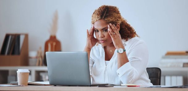 Young serious mixed race businesswoman looking stressed working on a laptop alone in an office at work. Hispanic woman unhappy while reading an email. Businessperson looking tired and worried. - Foto, afbeelding