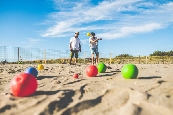 Touristen spielen ein aktives Spiel, Boule am Sandstrand am Meer - Gruppe junger Leute spielt in den Strandferien draußen Boule - Bälle auf dem Boden - Foto, Bild