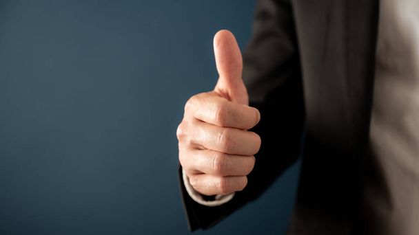 Businessman showing a thumbs up gesture over blue background with copy space on the left side of the image. - Photo, image