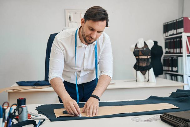 Estilista concentrado fica na sala de costura, enquanto a mão traça o padrão no material - Foto, Imagem