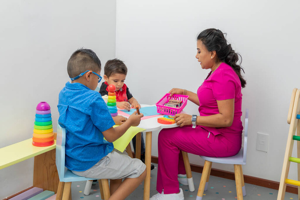 Latina Kinderärztin, spielt mit zwei Kindern an einem Tisch mit Spielzeug, in ihrem Büro - Foto, Bild