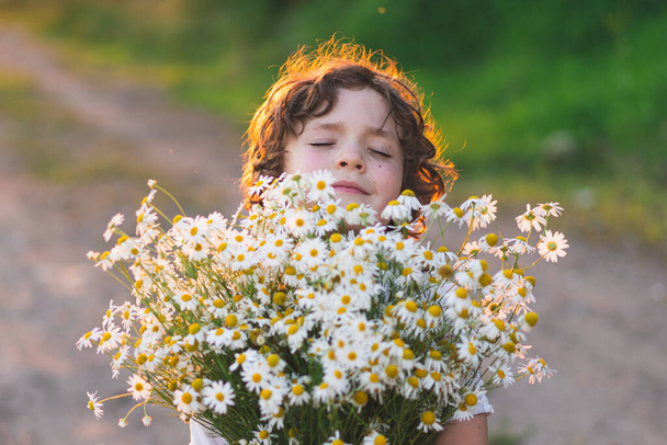 Милый улыбающийся мальчик на ромашковом поле на закате в мягком солнечном свете. Жизнь без аллергии, дышите свободно. Мальчик и маргаритки. Ребёнок мечтает и улыбается на фоне ромашкового поля. - Фото, изображение