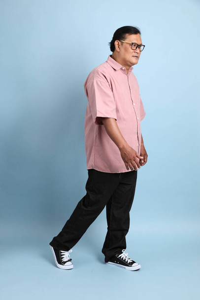 The adult Asian man with pink shirt standing on the blue background. - Foto, afbeelding