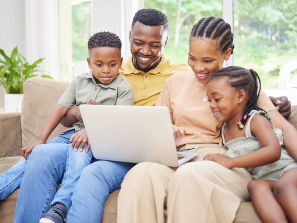 Foto de una familia joven sentada en el sofá juntos en casa y usando una computadora portátil. - Foto, Imagen