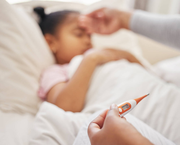 Sick little girl in bed while her mother uses a thermometer to check her temperature. Mixed race parent feeling daughters forehead. Hispanic child feeling ill and sleeping while mother checks fever. - Photo, image