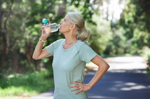 Shot of a mature woman drinking water while exercising outdoors. - Valokuva, kuva