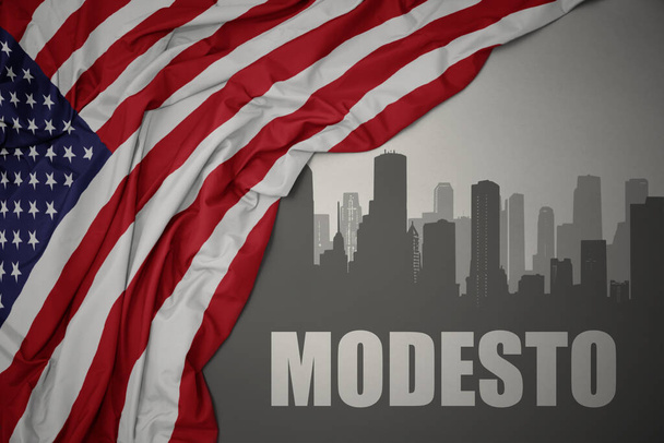 abstract silhouette of the city with text Modesto near waving colorful national flag of united states of america on a gray background. 3D illustration - Photo, Image