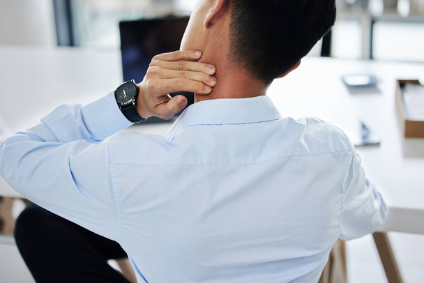 Rear view of a businessman experiencing discomfort while sitting at his desk. Unknown male suffering on neck pain while sitting at the desk in a office. - Foto, Imagem